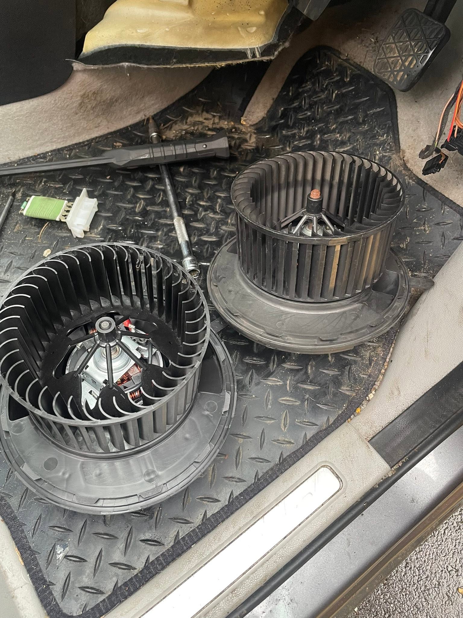 Two heater blower fans taken out of a car, resting in the footwell