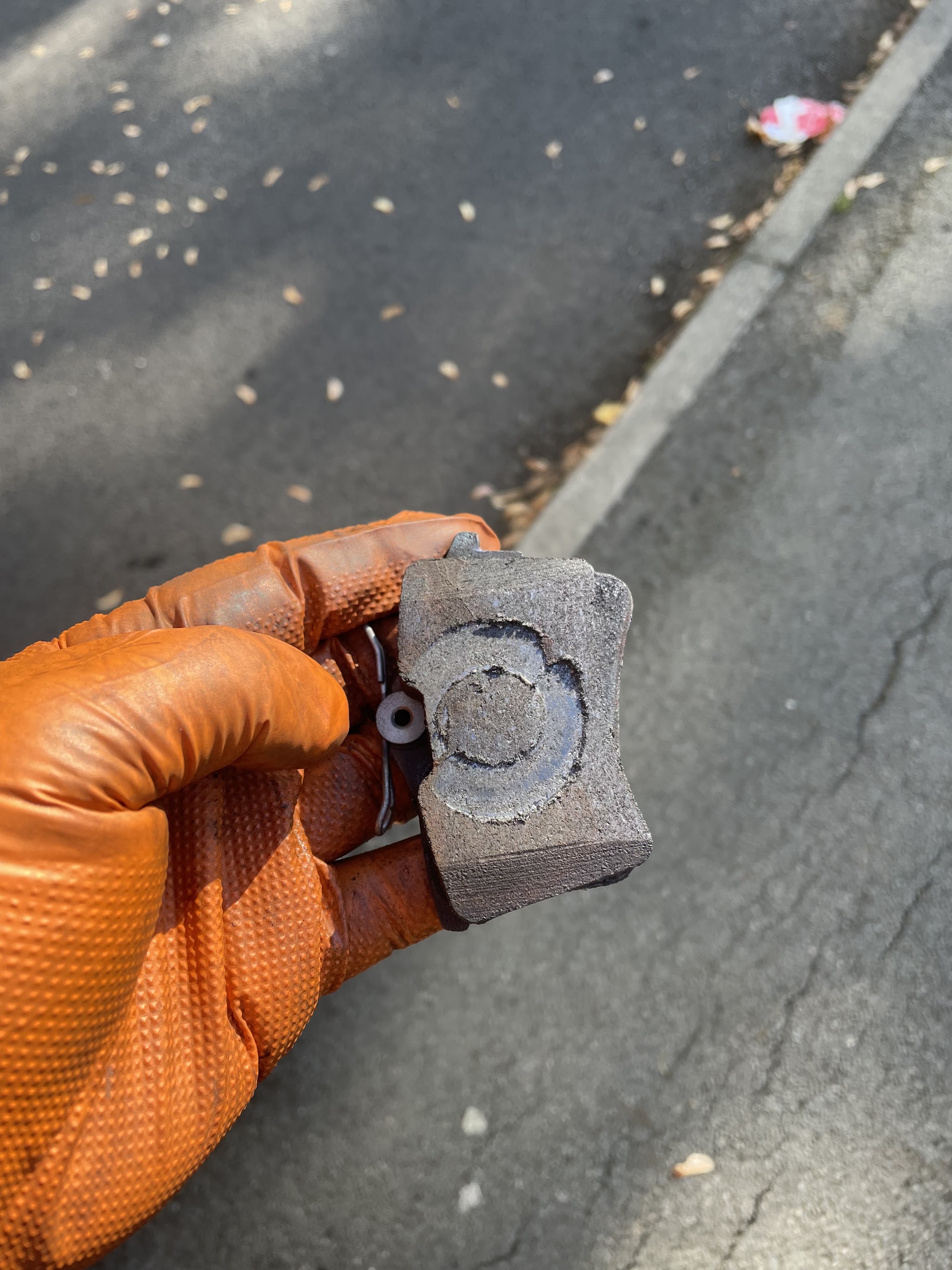 A gloved hand holding a worn brake pad over the road