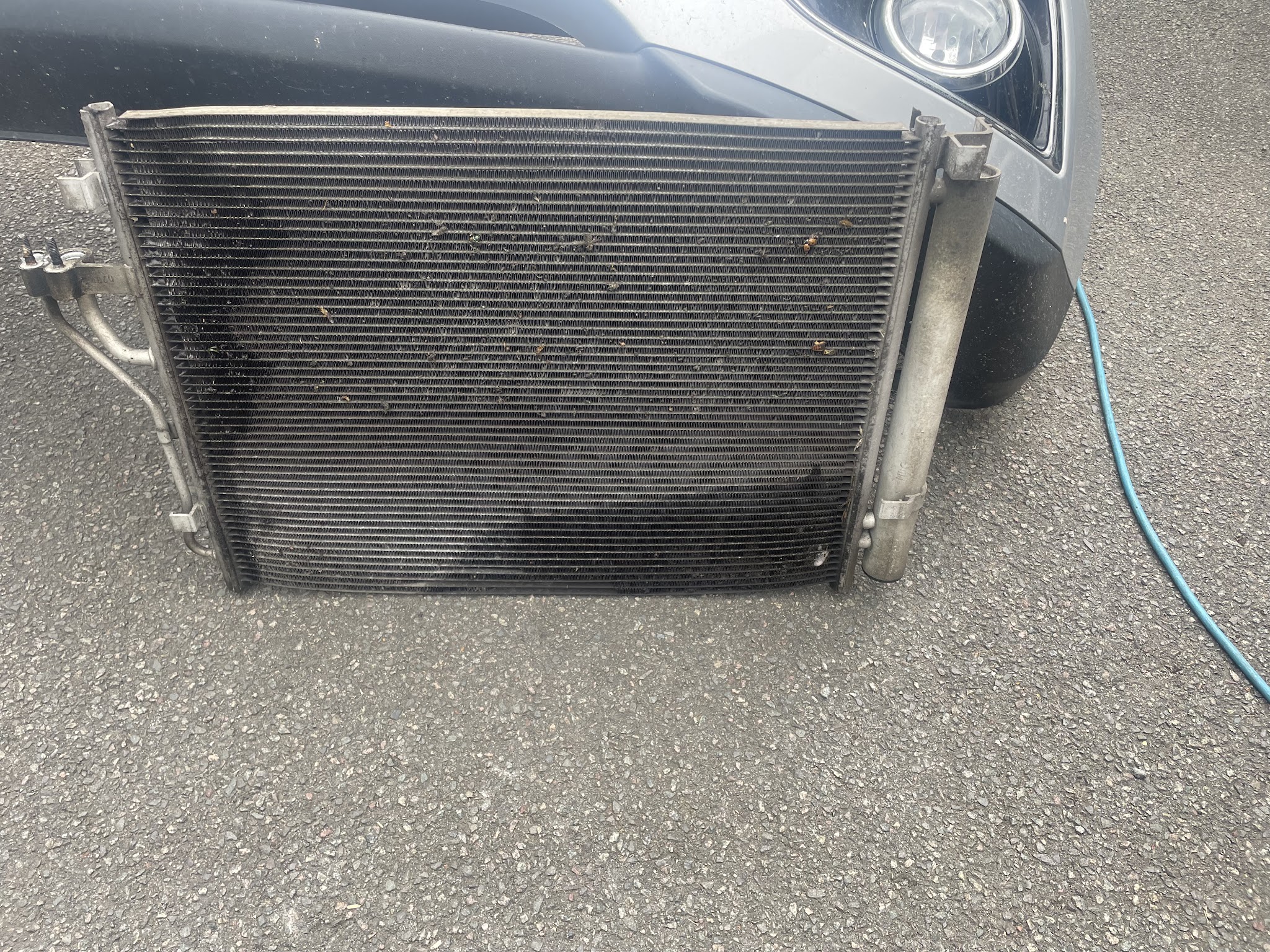 A radiator removed and laid on the driveway in front of the car